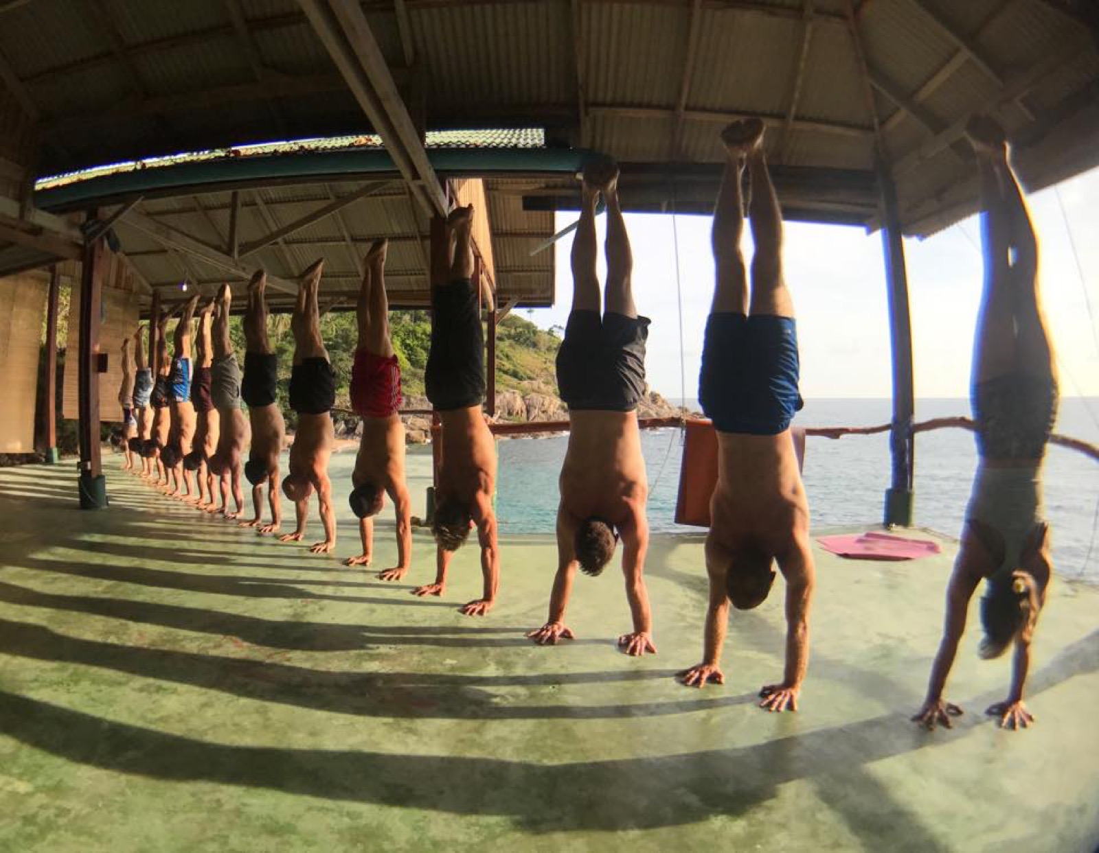 Workshop participants doing handstands in a line by the ocean in Thailand