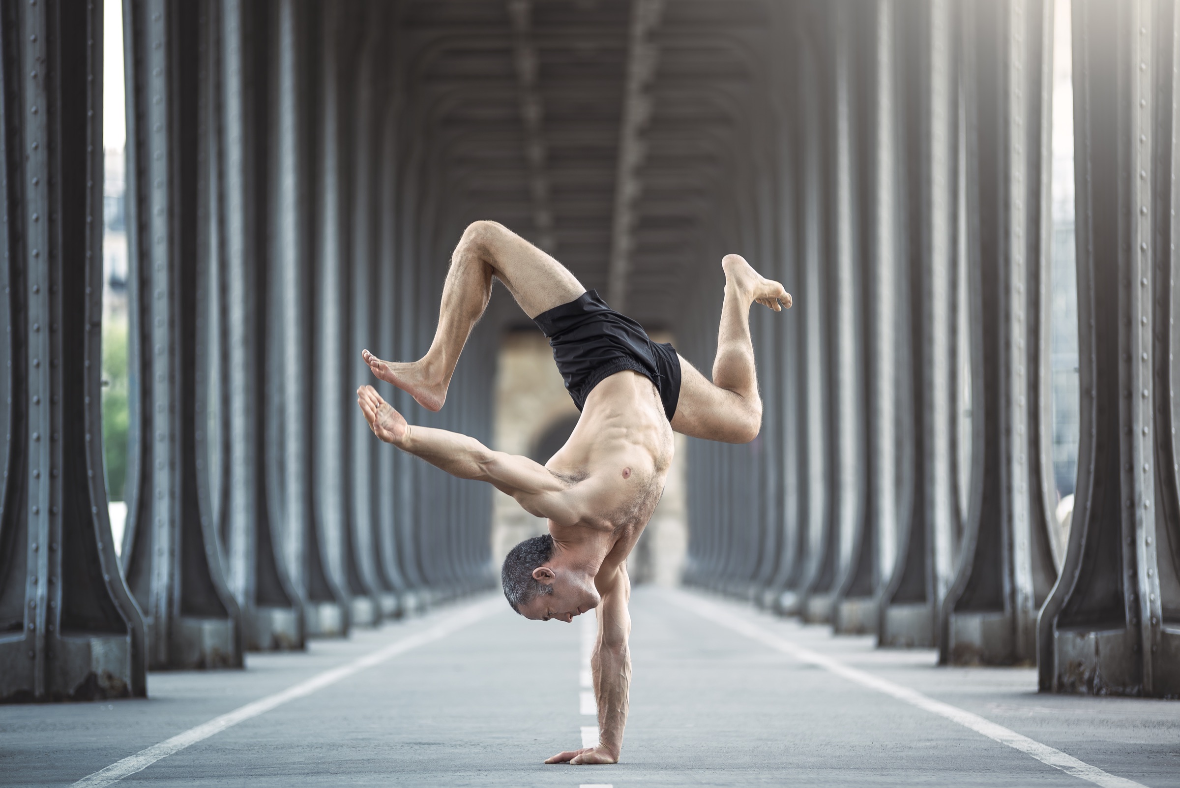 Yuval Ayalon performing a one-arm handstand between the columns of Pont de Bir-Hakeim in Paris